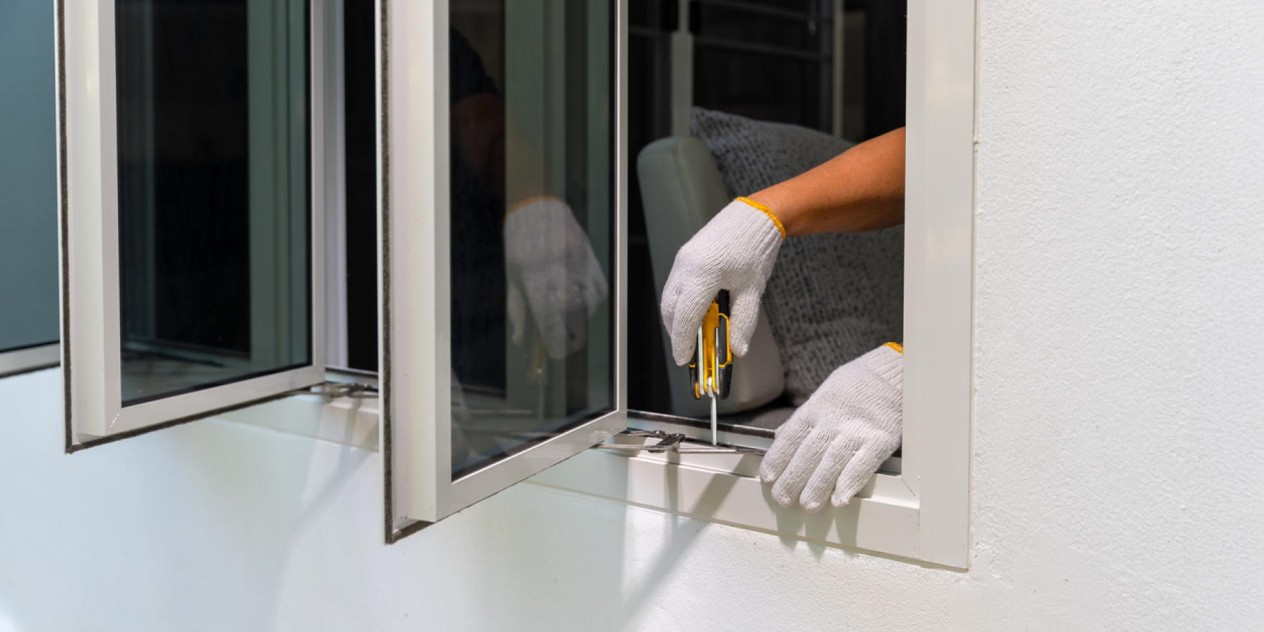 Worker wearing gloves uses a screwdriver to adjust a window hinge.